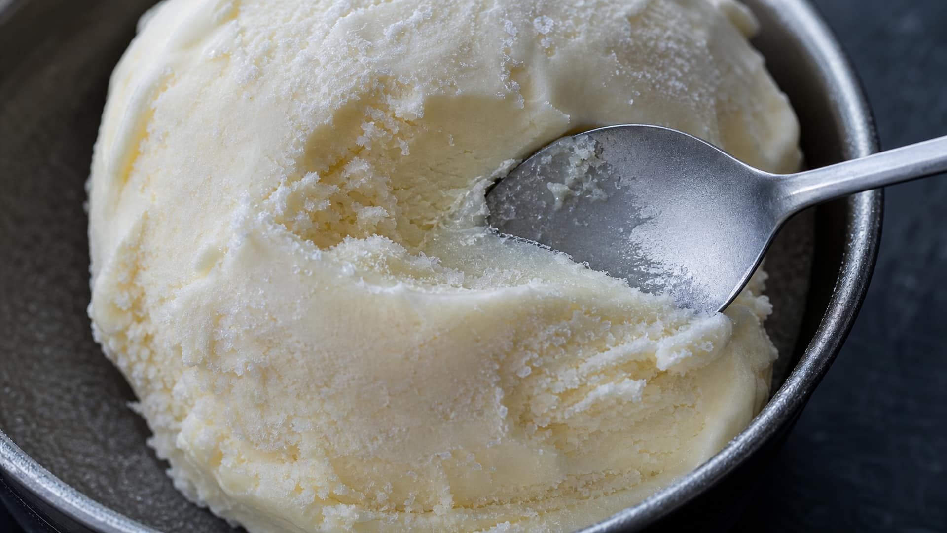 An icy ice cream scoop with coarse, visible ice crystals across a rough surface.