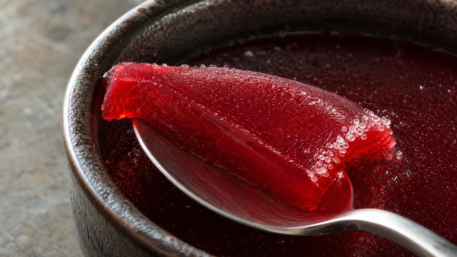 A translucent pâte de fruit gel holding a clean fold as a spoon lifts it.