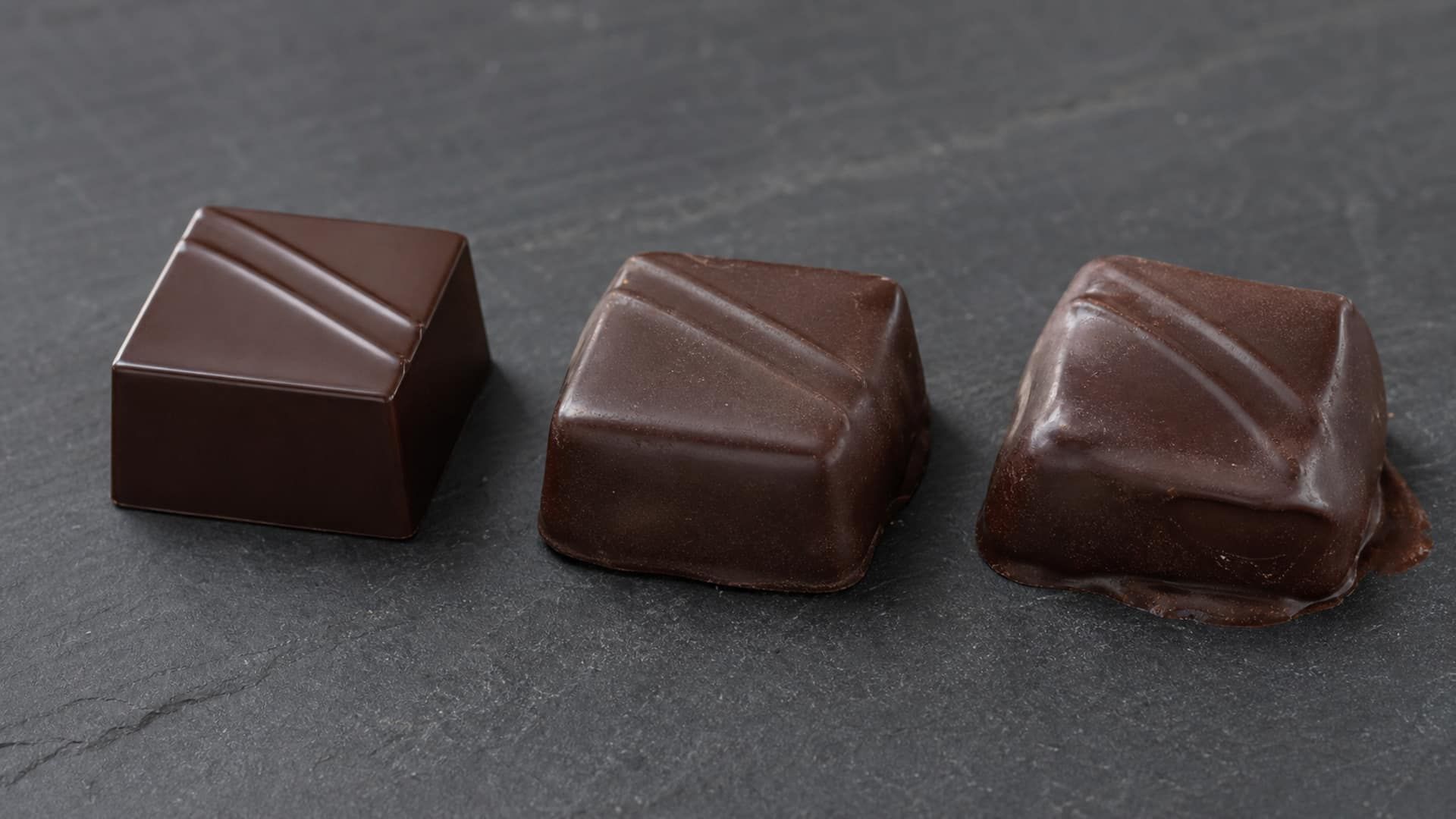 A chocolate bonbon softening and slumping, with a glossy melt pooling at its base.